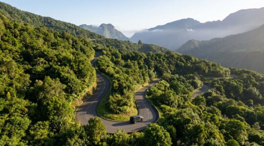 Vue panoramique d'une route sinueuse de montagne à La Réunion avec une voiture traversant un paysage tropical luxuriant
